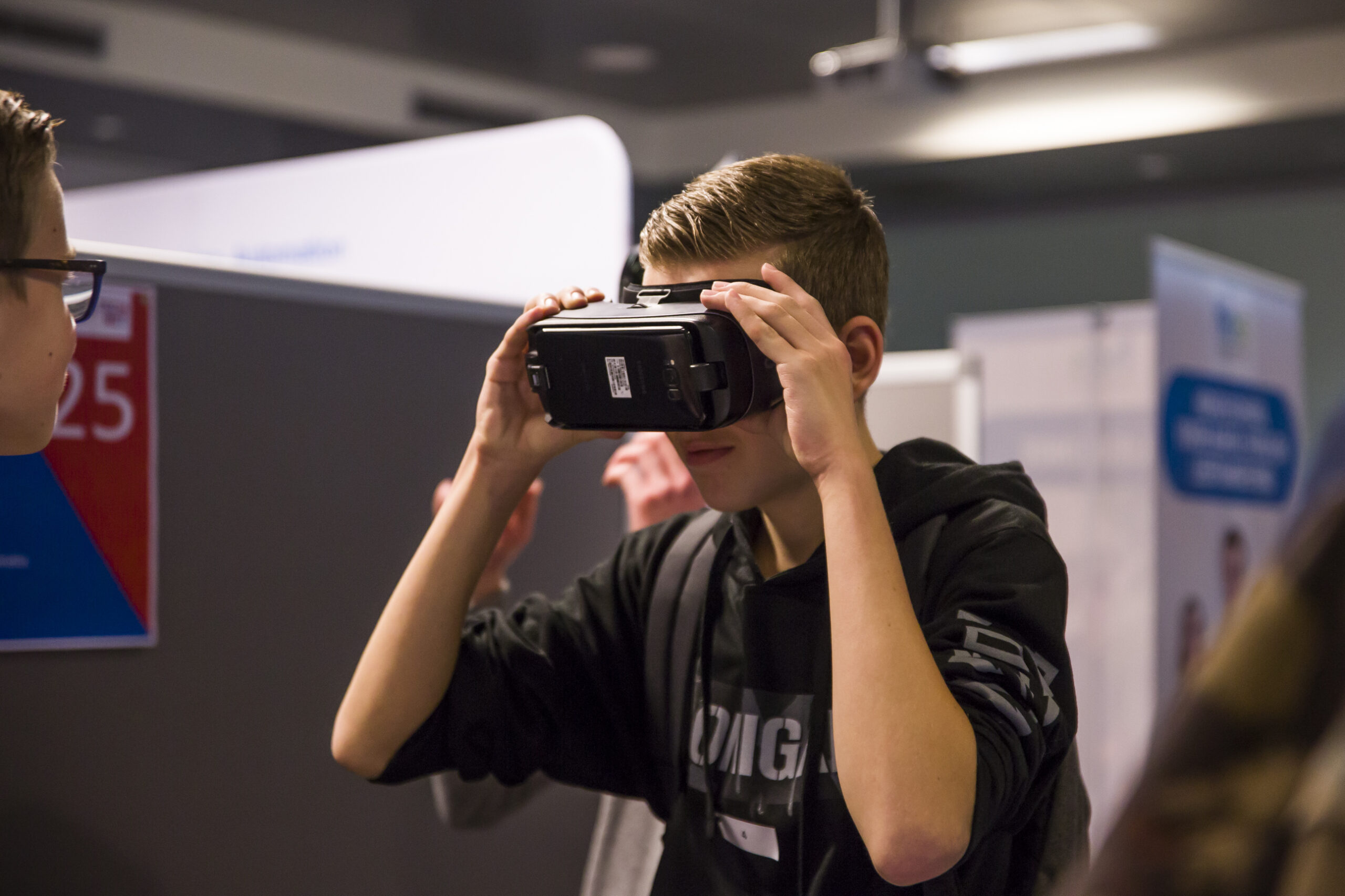 Een jongen in een donkere hoodie en met een rugzak om kijkt door een VR bril